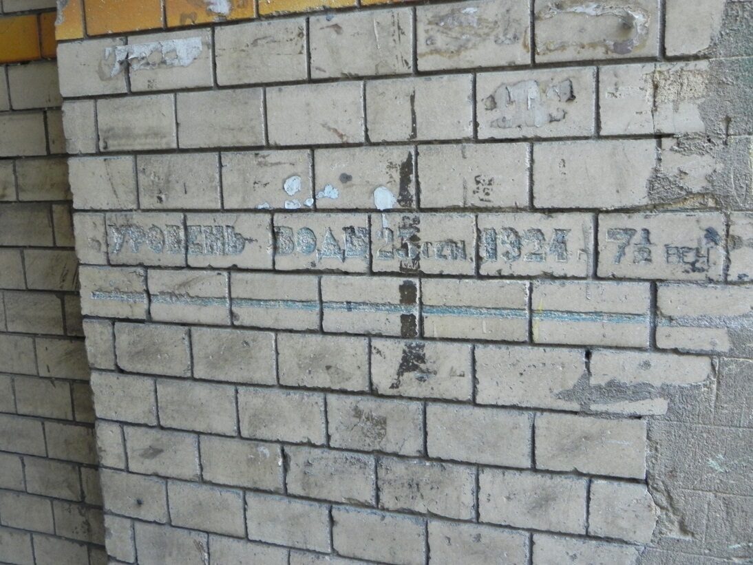 Крупный план надписи «Уровень воды 23 сен. 1924 г. 7½ веч.», процарапанной по облицовочной плитке, с горизонтальной бирюзовой чертой